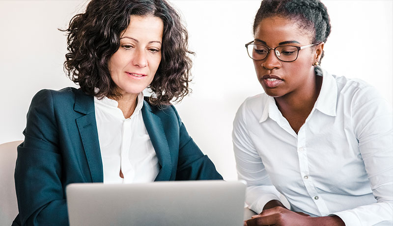 two female office workers sitting at a laptop