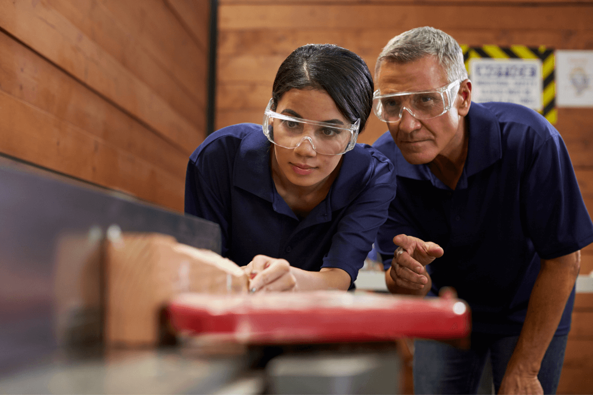 two woodworking employees looking closely at a saw