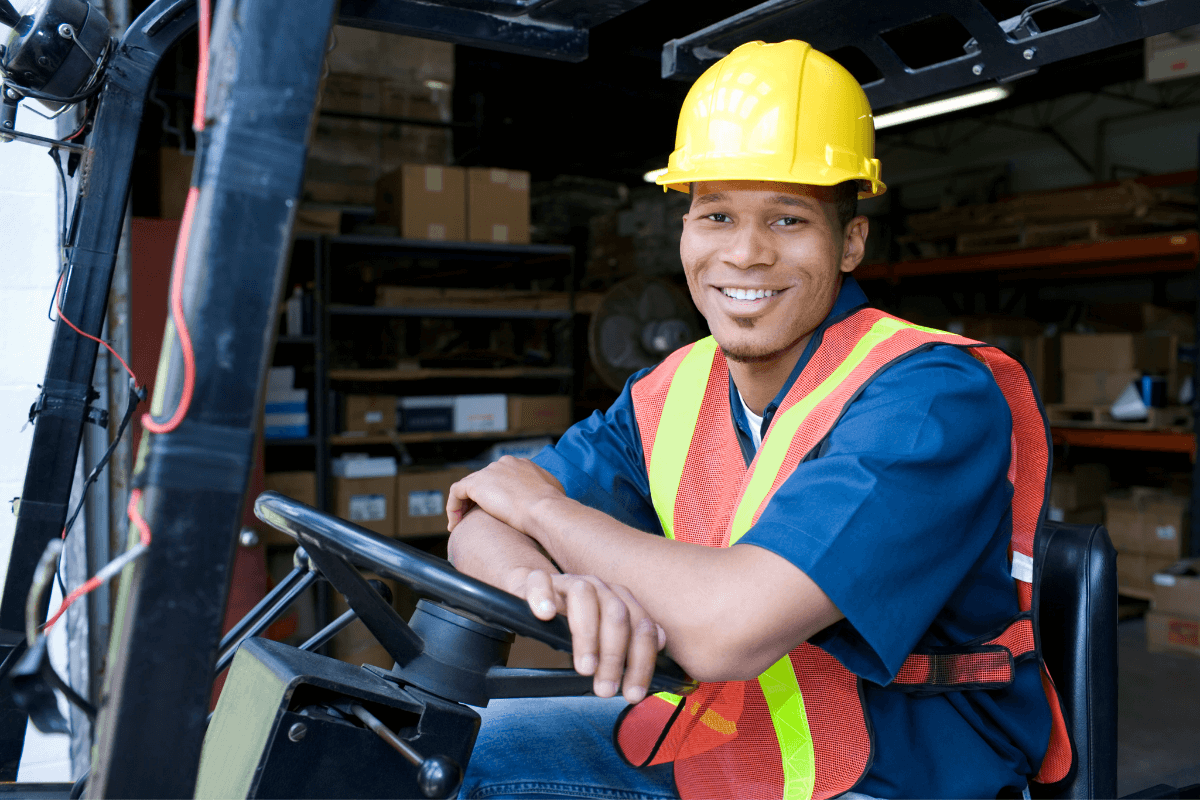 young man in a hard hat and vest sitting on a forklift