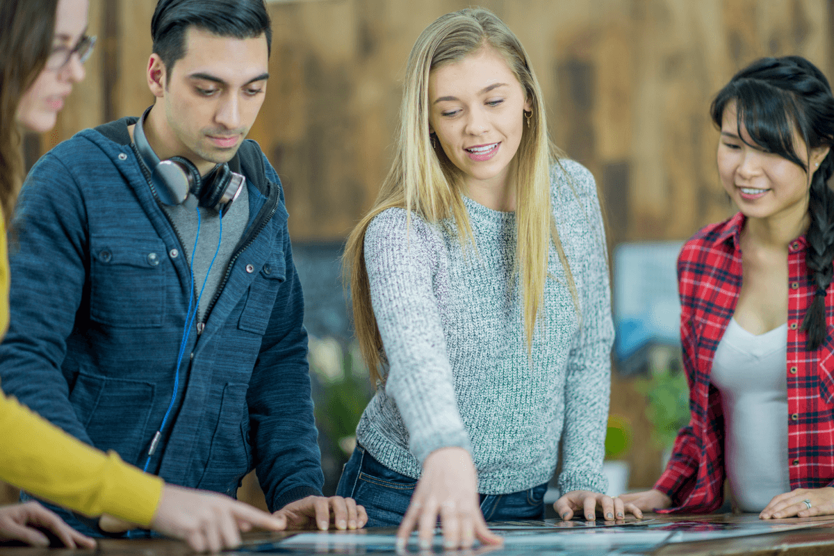 four young students looking at a print out on a table